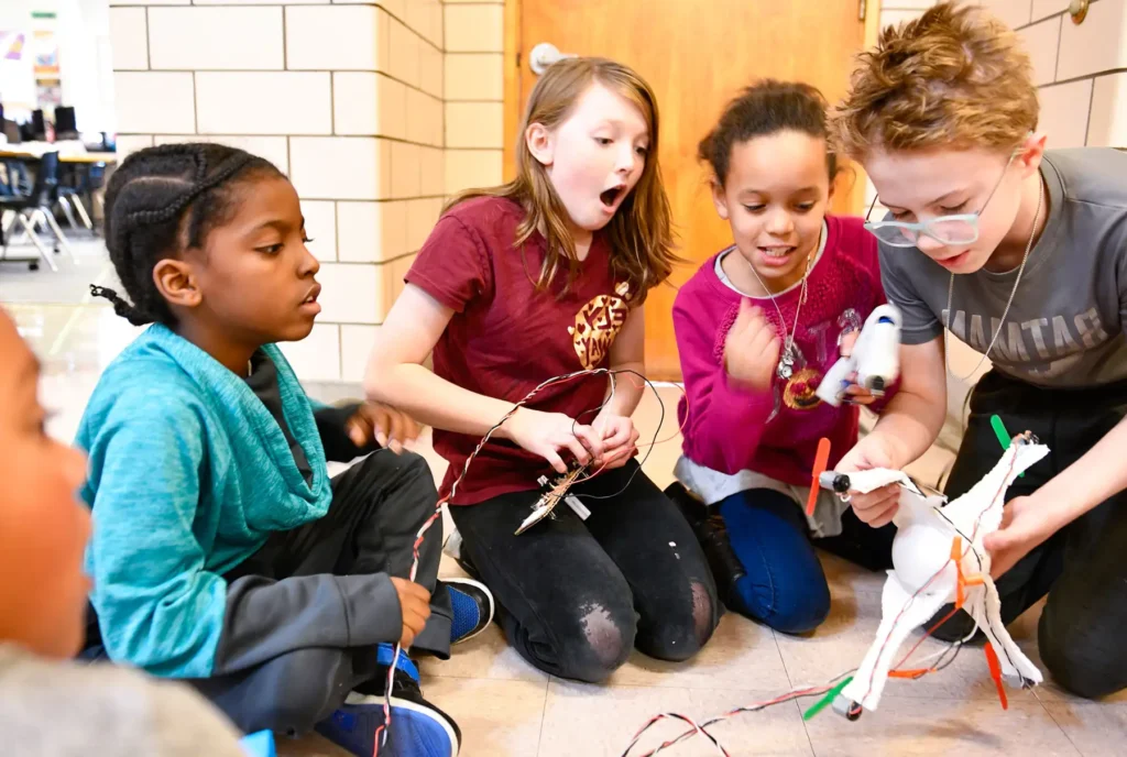 A group of four students look in awe as they connect wires to a robot.