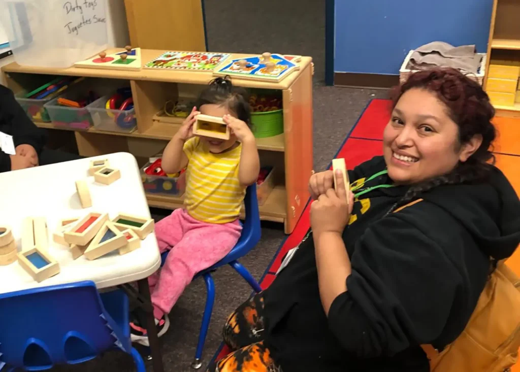 Daughter at children's table playing with blocks with her mom in the classroom.