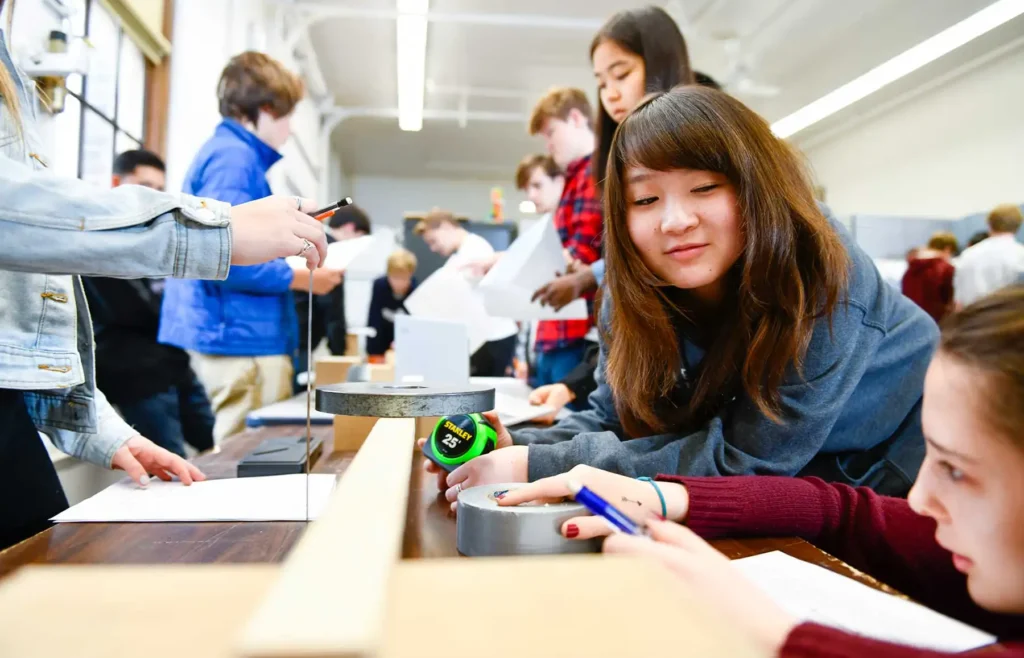 Two students work on a science project involving wood and duct tape.