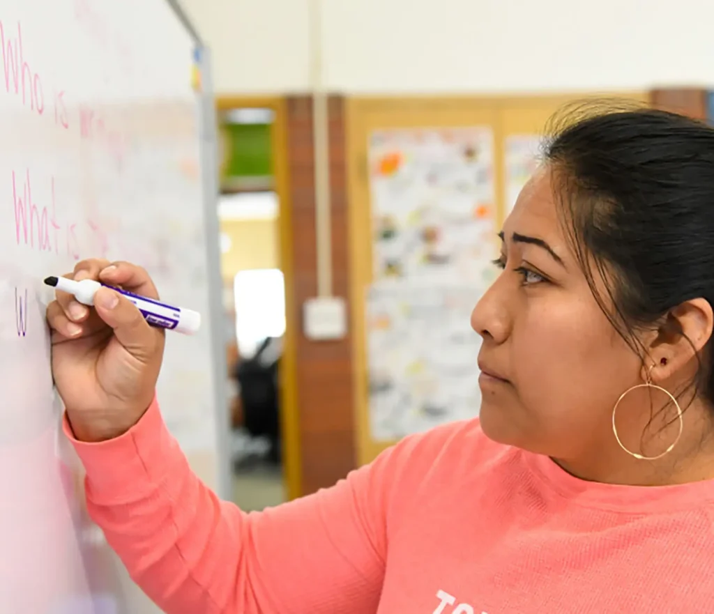 A young woman writes on a whiteboard with a purple dry erase marker.