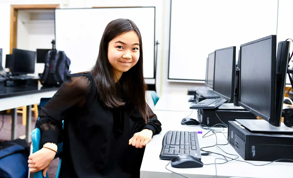 A young girl sits alone in a computer lab.