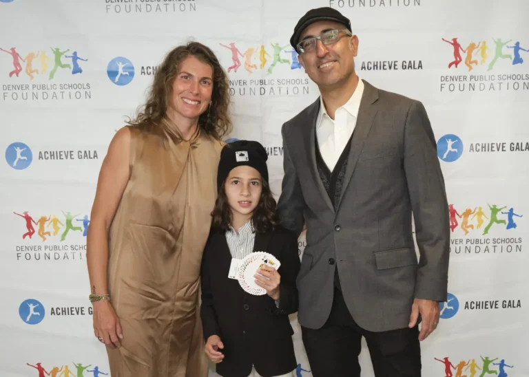 Two middle aged adults pose with a young magician doing a card trick in front of the 2024 Achieve Gala backdrop.