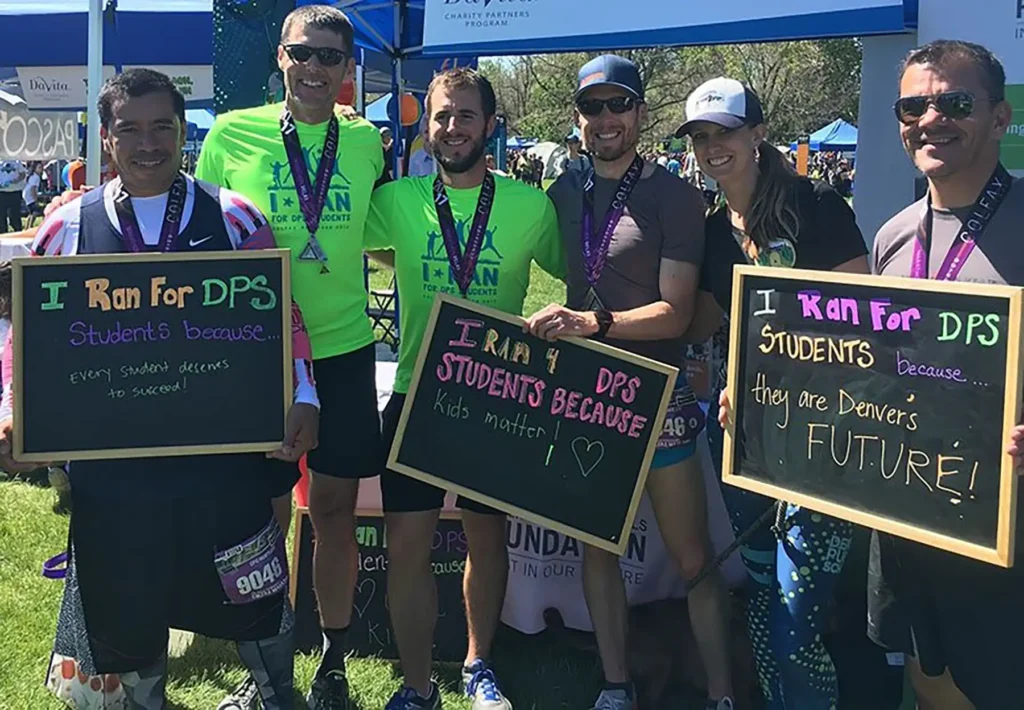 A group of runners at the Colfax Marathon holding up chalkboards that describe their reasons for running for DPS Students.