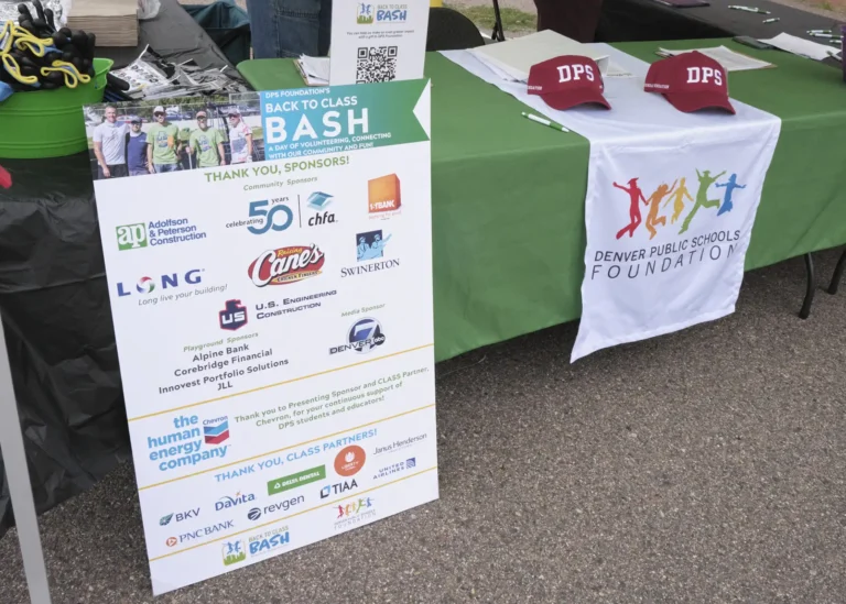 An information table with a large poster that lists out the sponsors and partners of the Back to Class Bash. There are also working gloves and hats on the table.