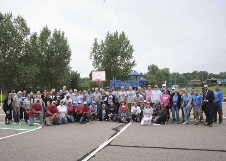 A large group of volunteers pose at the outdoor basketball court of a school for the Back to Class Bash.