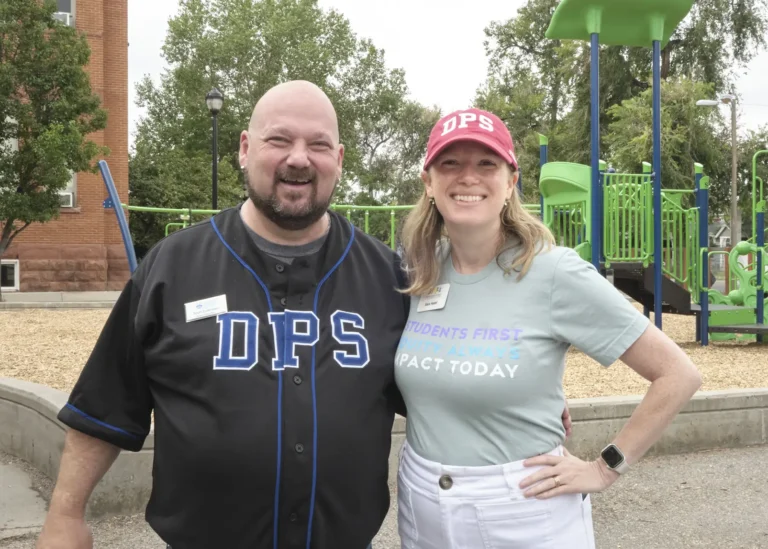 A white man and woman pose in front of a school playground for the Back to Class Bash.