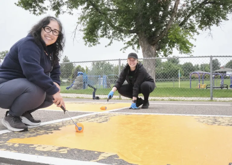 Two volunteers paint the pavement a bright orange color.