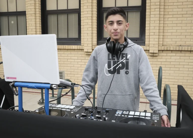 A young DJ wearing headphones around his neck works at a DJ mixer.