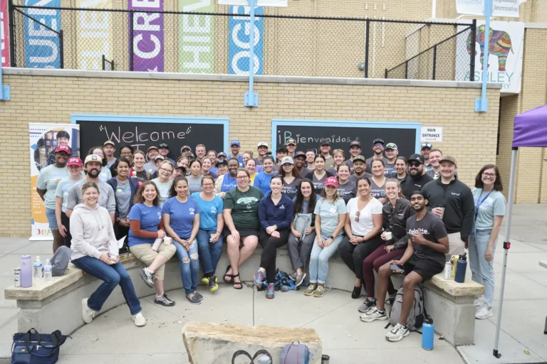 A large group of volunteers pose outside of a school for the Back to Class Bash.