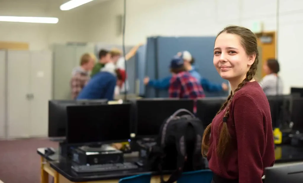 A high school aged student with two braids smiles in a classroom.