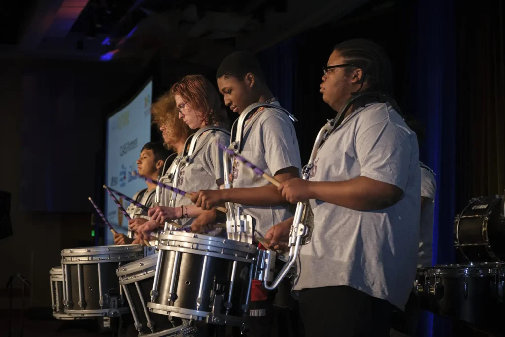 A group of high school aged drummers form a drum line on stage at the 2024 Achieve Gala.