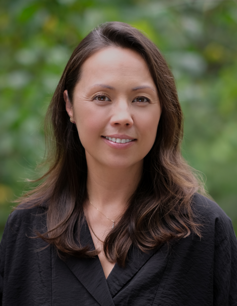 Headshot of Jenny smiling outdoors in front of greenery, wearing a black blouse.