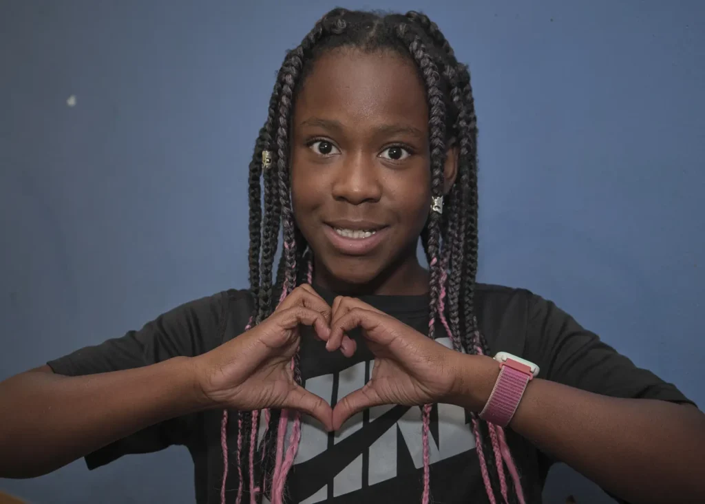 A young black girl forms a heart with her hands in her classroom.