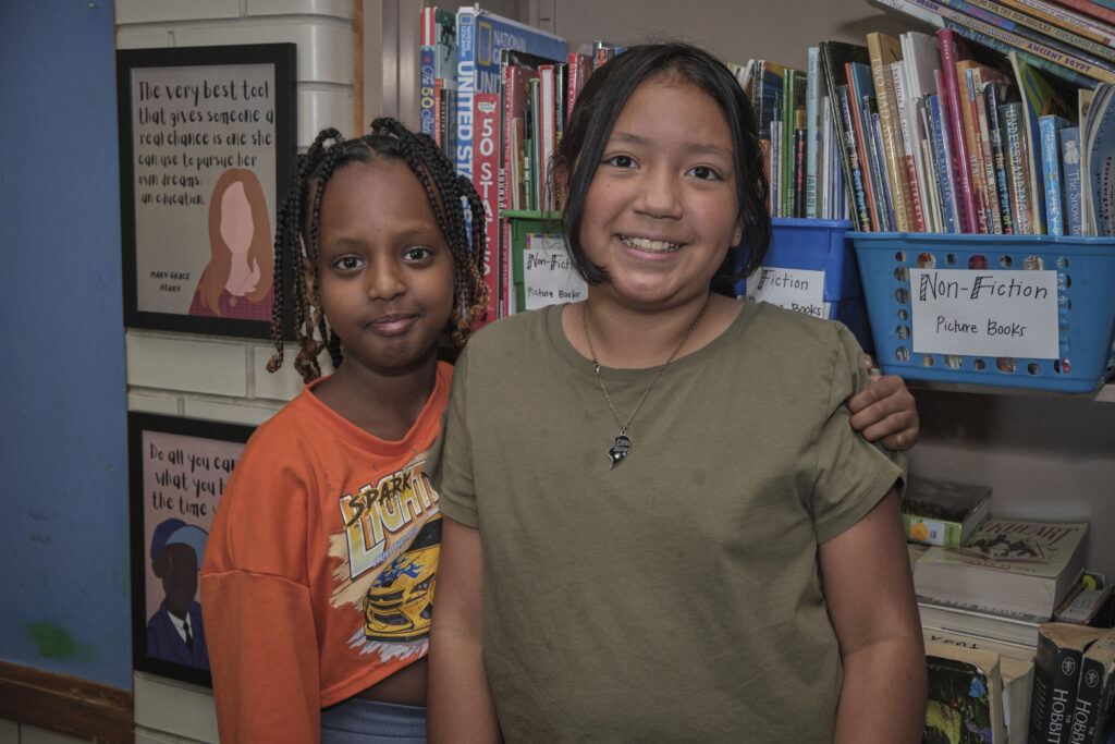 Two children smiling in front of a book shelf.