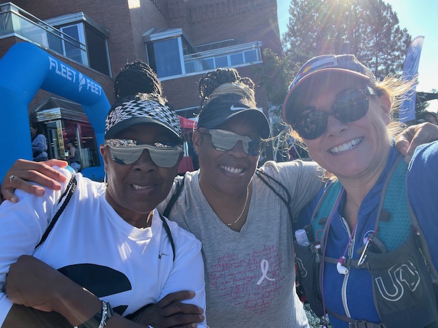 3 women in running gear pose together at the finish line at a race