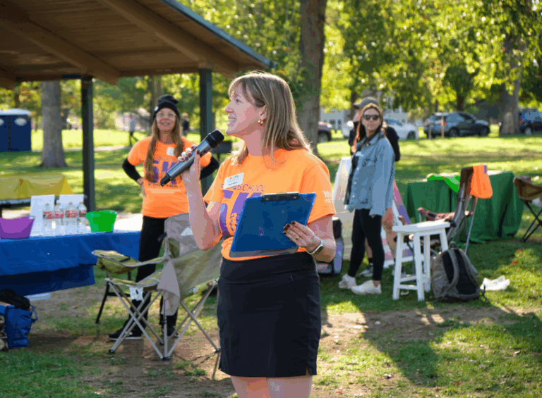 DPS Foundation CEO Sara Hazel speaks to participants, holding a microphone and clipboard.