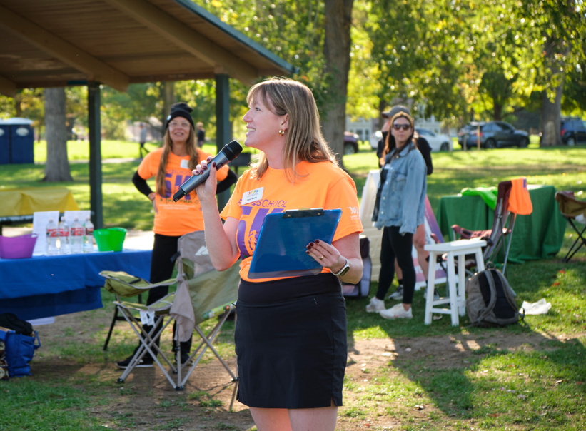 DPS Foundation CEO Sara Hazel speaks to participants, holding a microphone and clipboard.
