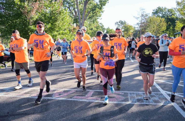 Runners take off from the start line at the Back to School 5K Fun Run, wearing bright orange shirts and smiles.