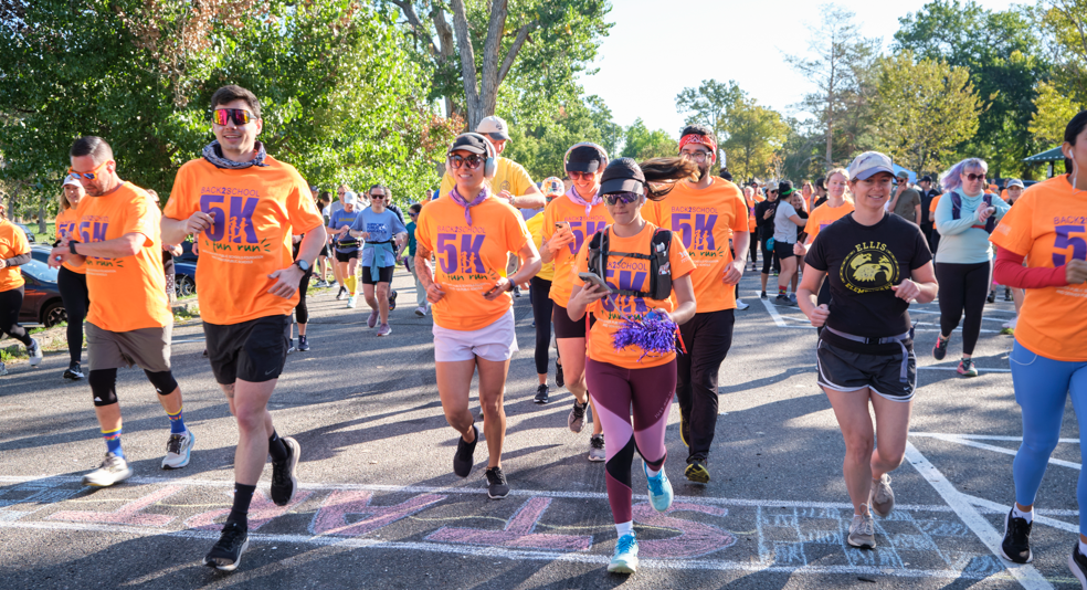 Runners take off from the start line at the Back to School 5K Fun Run, wearing bright orange shirts and smiles.