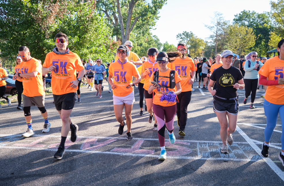 Runners take off from the start line at the Back to School 5K Fun Run, wearing bright orange shirts and smiles.