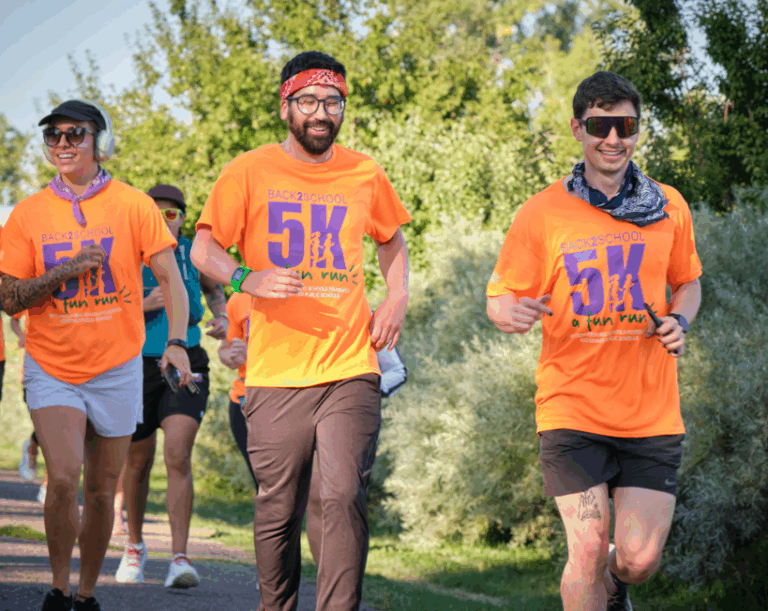 Participants smile as they run, wearing bright orange event shirts.