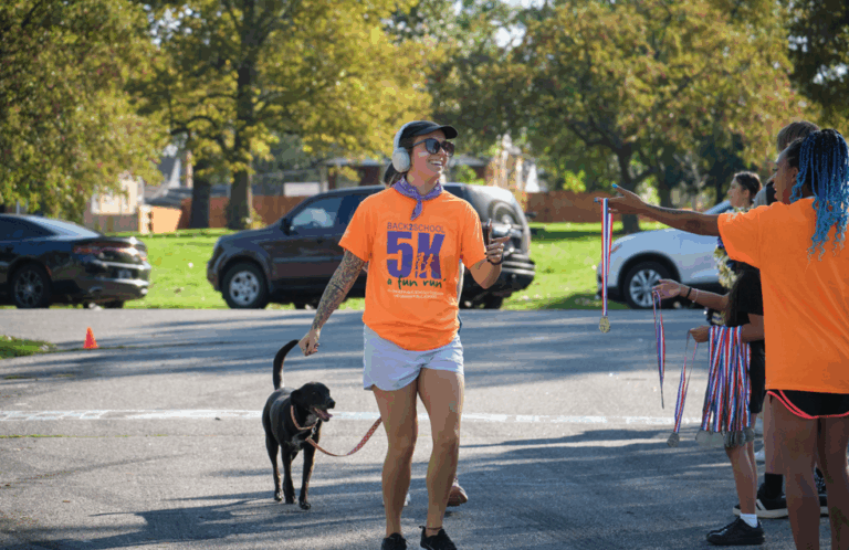 Participant finishes the race alongside their dog while receiving a medal.
