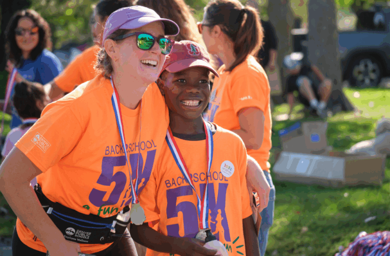 Two participants smiling proudly after completing the Back to School 5K Fun Run, wearing bright orange event shirts and medals.