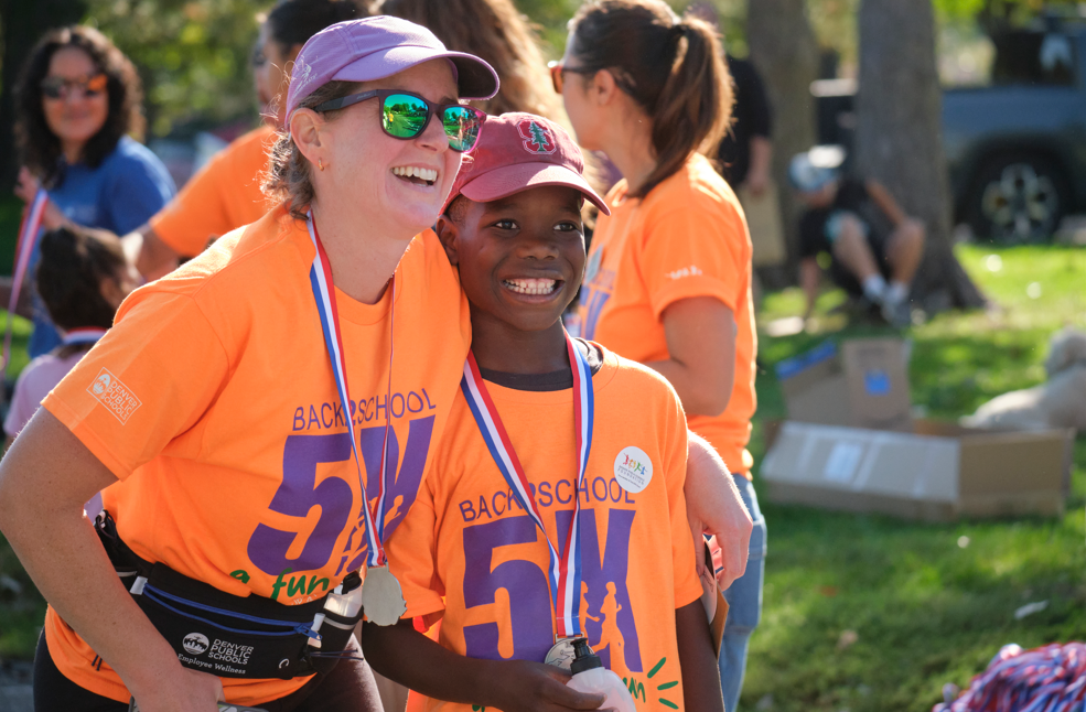 Two participants smiling proudly after completing the Back to School 5K Fun Run, wearing bright orange event shirts and medals.