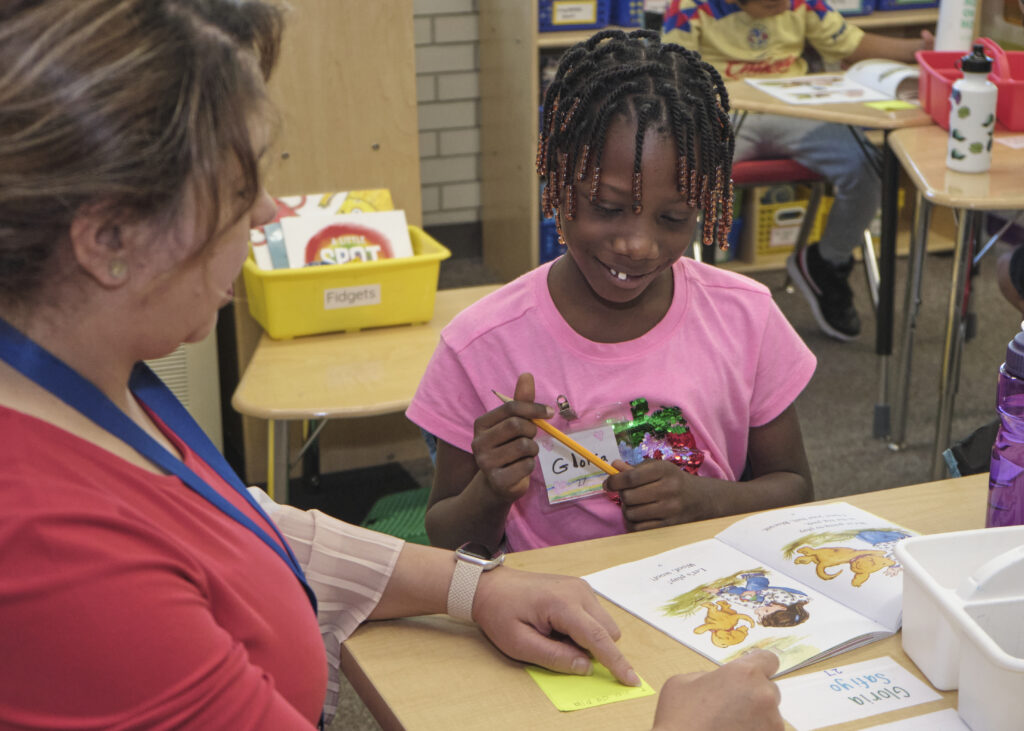 Image of a teacher and a student sitting at a desk reading.