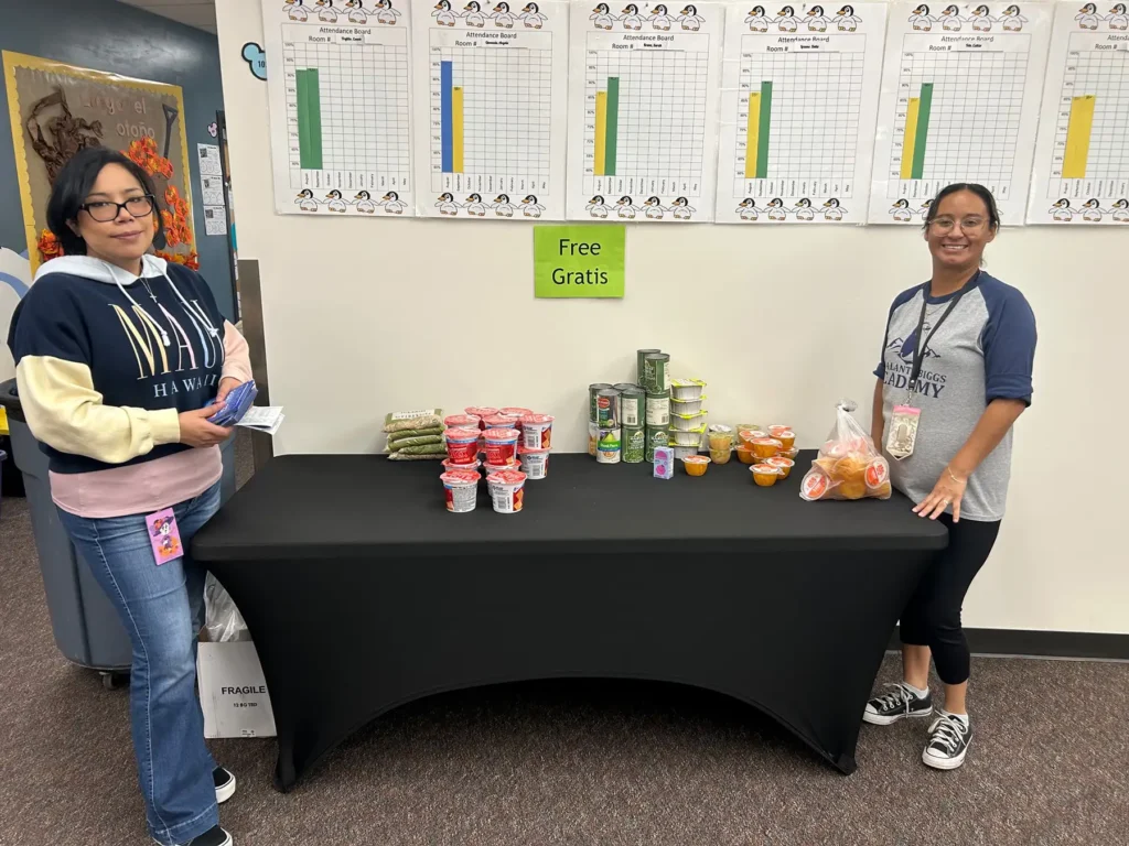 Two women standing beside a table with food pantry items and a sign that says "free"