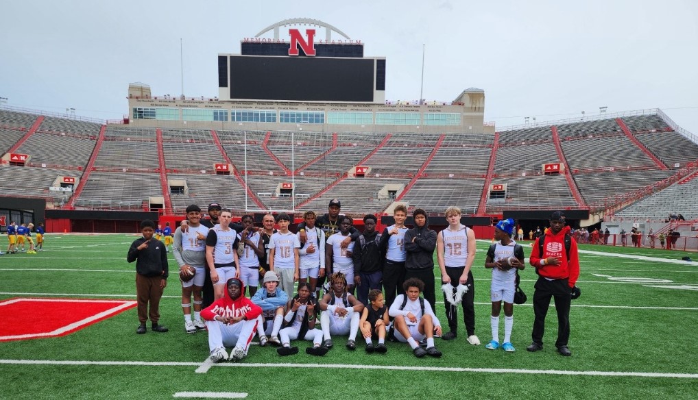 A group of football players posing together on a football field inside a large stadium.