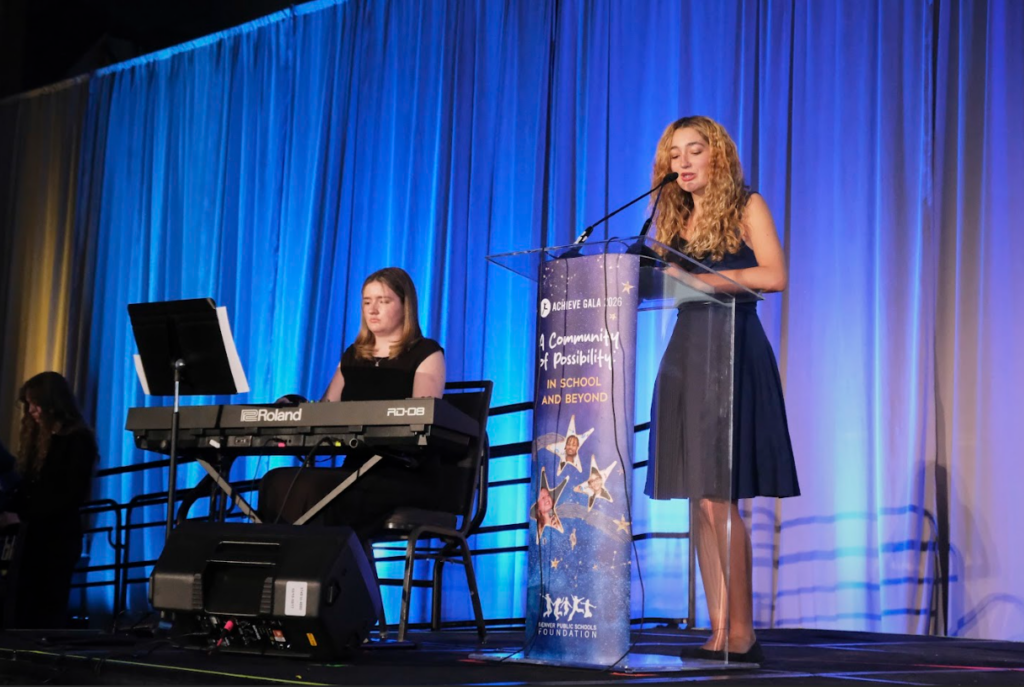 Student speaking at podium while another student plays keyboard at Achieve Gala 2026.