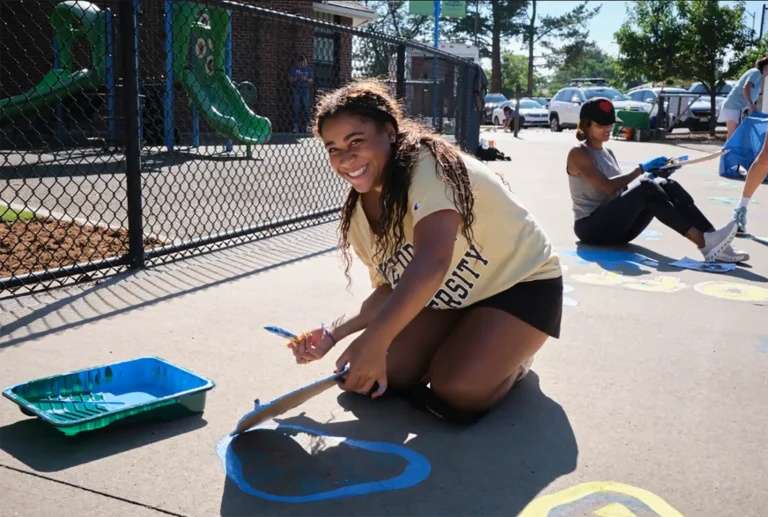 A girl paints a paw print on the concrete at a school for the day of service