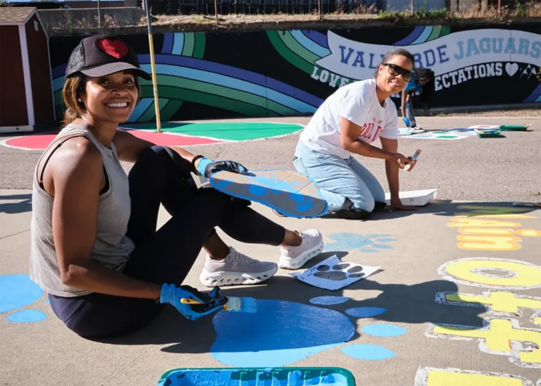 Two women work to paint paw prints on a schools parking lot for a service daw